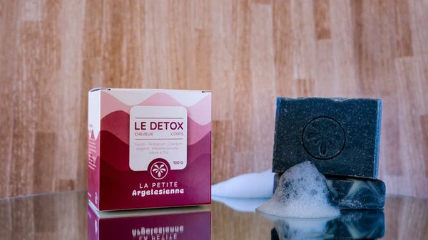 Savon solide artisanal naturel Le Détox pour le corps et les cheveux, présenté avec son emballage et une mousse naturelle