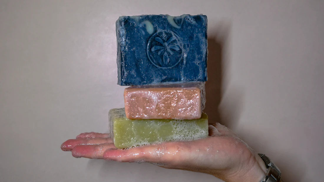 Savons solides artisanaux naturels de différentes couleurs, présentés en main avec mousse lors de l’utilisation